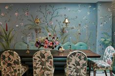 a dining room table and chairs in front of a wall with flowers painted on it