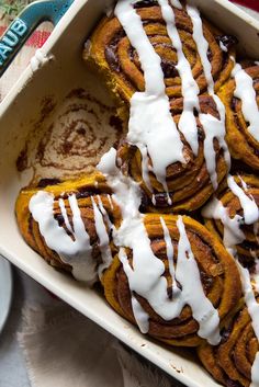 a pan filled with cinnamon rolls covered in white icing and drizzled