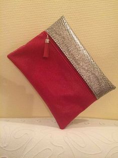 a red and silver purse sitting on top of a white bed next to a wall