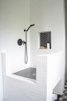 a white tiled bathroom with black and white tiles on the shower head, toilet paper in the corner