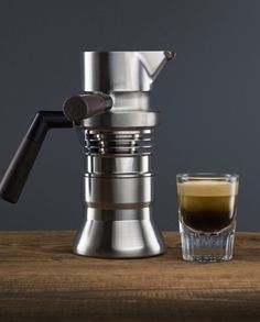 an espresso machine next to a shot glass on a wooden table with a gray background