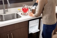 a woman is pouring water into a cup in the kitchen sink while holding a strainer