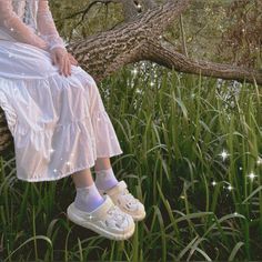 a woman is sitting on a tree branch in the grass wearing tennis shoes and socks