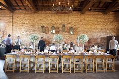 a group of people standing around a table with plates and glasses on it in front of a brick wall