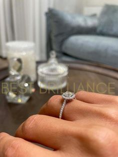 a woman's hand with a diamond ring on top of her finger, in front of a couch