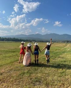 three girls in dresses and hats walking across a field