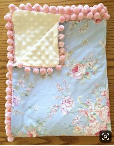 a pink and blue blanket with pom - poms on the edge, sitting on a wooden table