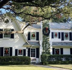 a large white house with black shutters and wreaths on the front door is decorated for christmas