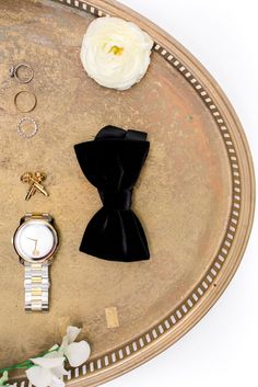 an assortment of jewelry on a tray with white flowers and black ribbon around the edges