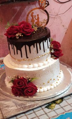 a three tiered cake with chocolate frosting and red roses on top is sitting on a table