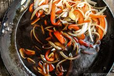 onions, carrots and peppers cooking in a wok on a wooden table top