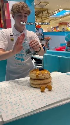 a young man is pouring water over a stack of pancakes on a table in a mall