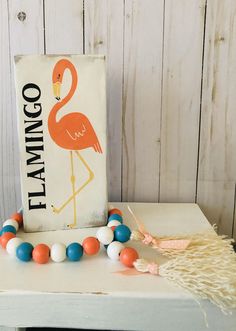 a flamingo sign sitting on top of a table next to beads and tassels