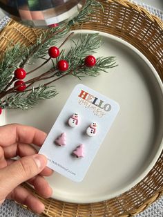 someone is holding up some christmas decorations on a plate next to a branch with red berries