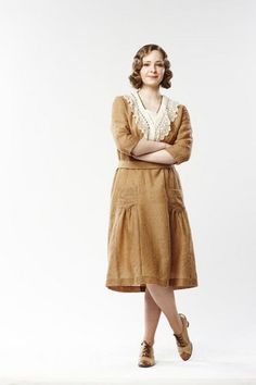 a woman standing with her arms crossed wearing a brown dress and shoes, in front of a white background