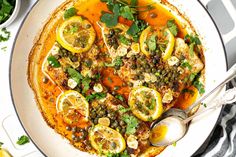 a white bowl filled with soup and topped with lemons, capers and herbs