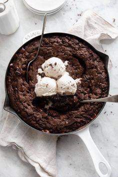 a chocolate cake with ice cream on top in a skillet next to a cup of coffee