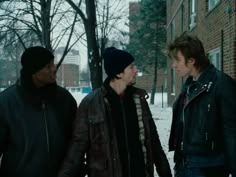 three young men standing next to each other in front of a brick building on a snowy day