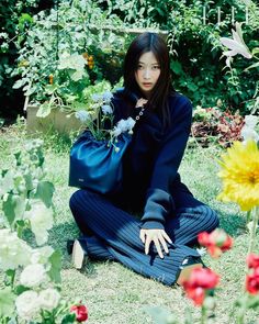 a woman sitting on the ground with flowers in her hand and wearing a blue outfit