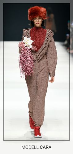 a model walks down the runway in a red hat and brown outfit with flowers on it