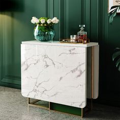 a marble cabinet with flowers on top in a living room area, next to a green wall