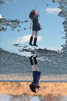 a reflection of a woman in the water with an umbrella over her head and boots on