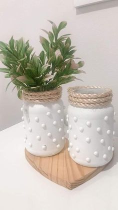 two white vases with plants in them sitting on a wooden stand next to each other