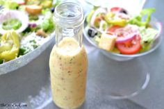 a bottle filled with dressing sitting on top of a table next to a bowl of salad