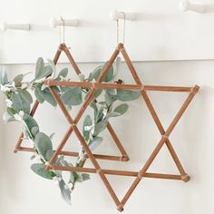 a star of david hanging on a wall with greenery in the foreground and white painted walls behind it