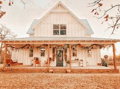 a white house with christmas decorations on the front porch and covered in garlands, surrounded by trees