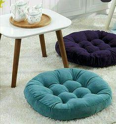 three round cushions on the floor next to a white table and two blue stools