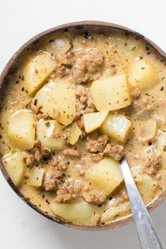 a bowl filled with meat and potatoes on top of a white table next to a spoon