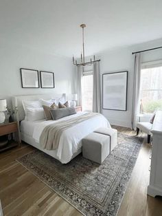 a large white bed sitting on top of a wooden floor next to a window covered in curtains