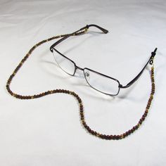 This eyeglass chain is made with genuine tigers eye beads and tarnish resistant gold plated beads.  The chain is 25" long.  Eyeglasses not included. Brown Glass Beaded Necklaces As Gift, Brown Glass Beaded Necklaces For Gifts, Adjustable Brown Glass Necklace, Adjustable Gold Beaded Copper Necklace, Gold Adjustable Single Strand Glasses Chain, Handmade Gold Glasses Chains With Round Beads, Gold Beaded Glasses Chains, Gold Glass Beaded Chain Necklaces, Gold Single Strand Adjustable Glasses Chain