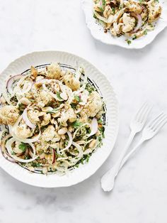 two white plates filled with food on top of a marble table next to utensils