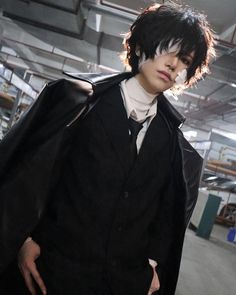 a man with black hair wearing a suit and tie in an industrial building, looking at the camera