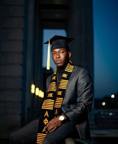 a man wearing a graduation cap and gown sitting on a ledge in front of a building