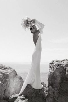 a woman standing on top of a rocky cliff next to the ocean wearing a long white dress