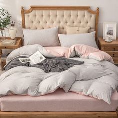 an unmade bed with pink and grey sheets, pillows and blankets on top of it