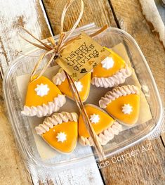 four orange and white decorated cookies in a plastic container with a tag on the top