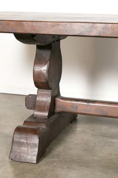 an old wooden table with two legs on concrete floor next to white wall and cement floor