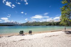 two lawn chairs sitting on top of a sandy beach next to the ocean with mountains in the background