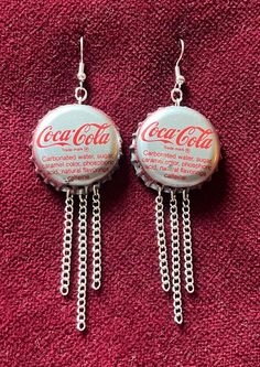 two coca cola bottle caps with chains hanging from them on a red surface, one has the