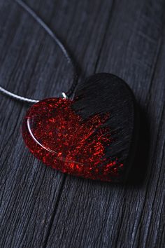 a red heart shaped pendant on a black wooden table with a chain hanging from it