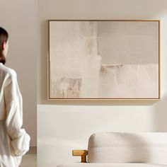 a woman standing in front of a white couch with a painting on the wall behind her