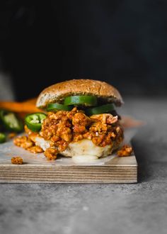 a sloppy joe sandwich with pickles and peppers on a cutting board, ready to be eaten