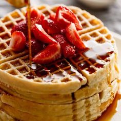 a stack of waffles topped with strawberries and syrup