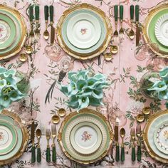 the table is set with plates, silverware and green flowers on pink wallpaper