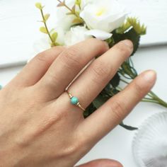 a woman's hand with a ring on it and flowers in the background,