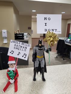 an elf and batman figurines are on the counter in front of a sign that says no i don't